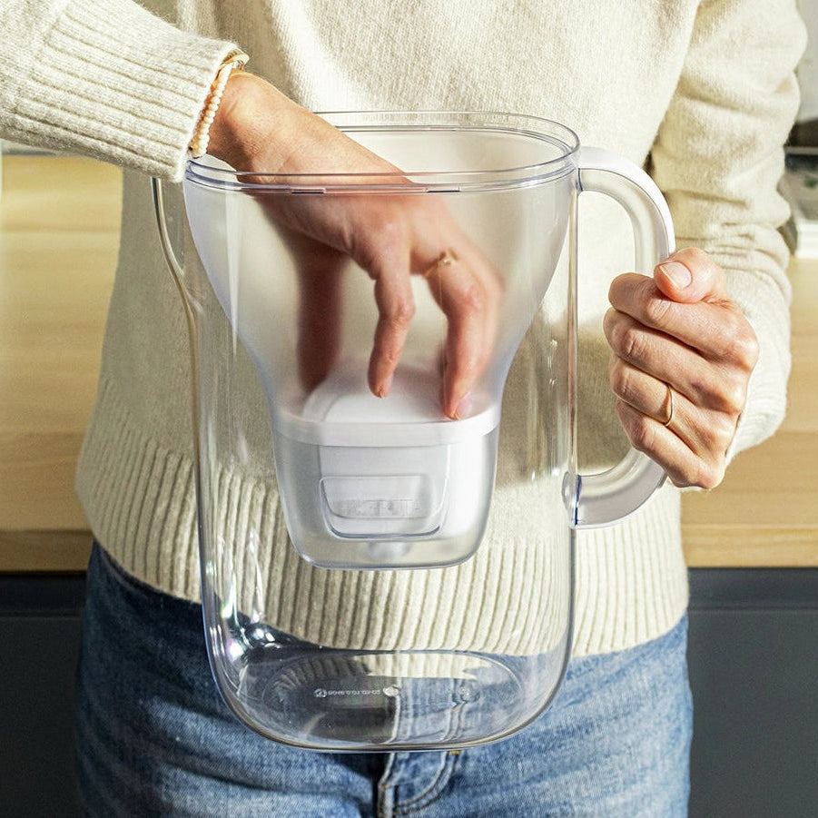 Une personne en pull blanc en train d'insérer un MAXTRA PRO filtre cartouche dans un BRITA Style Essential eau filtre cruche.