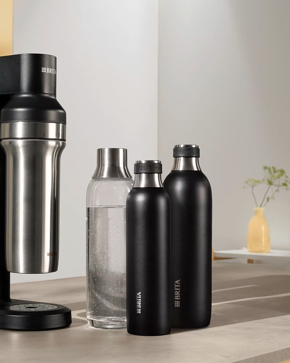 Black BRITA sodaTRIO Sparkling Water Maker displayed with BRITA sodaTRIO Glass and Stainless Steel Bottles on a countertop.