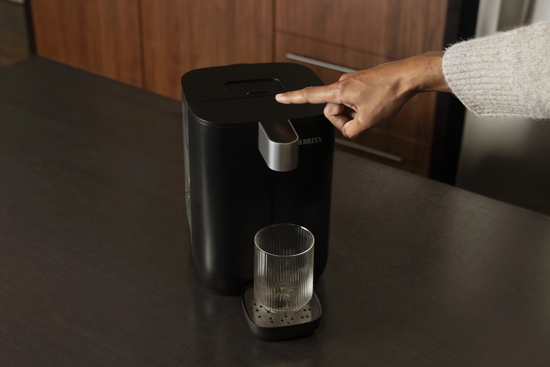 Person using the touch button on a BRITA YOURCE Mini water dispenser.